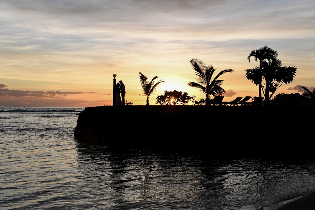 A silhouette of the palm trees, couple and the rocky dock against the fiery sunset