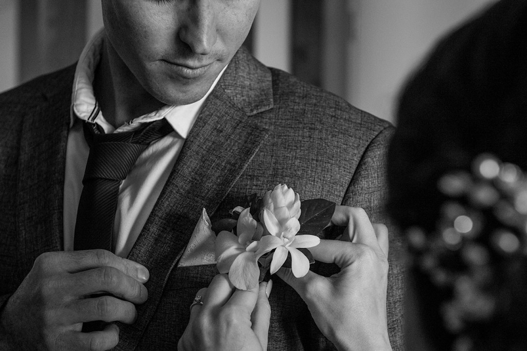 The bride adjusts the ginger flower boutonniere on her groom