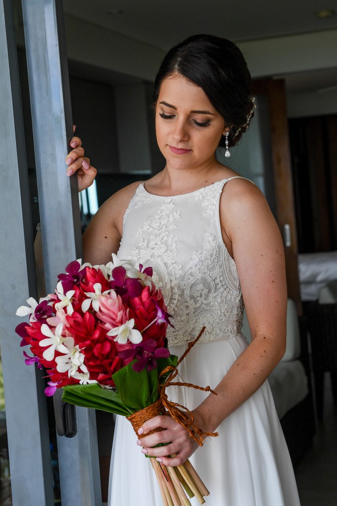 The bride stands in the doorway holding her stunning colourful island flower bouquet