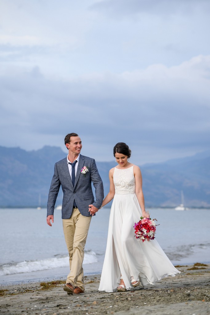 The newly married couple stroll on the beach against greying skies