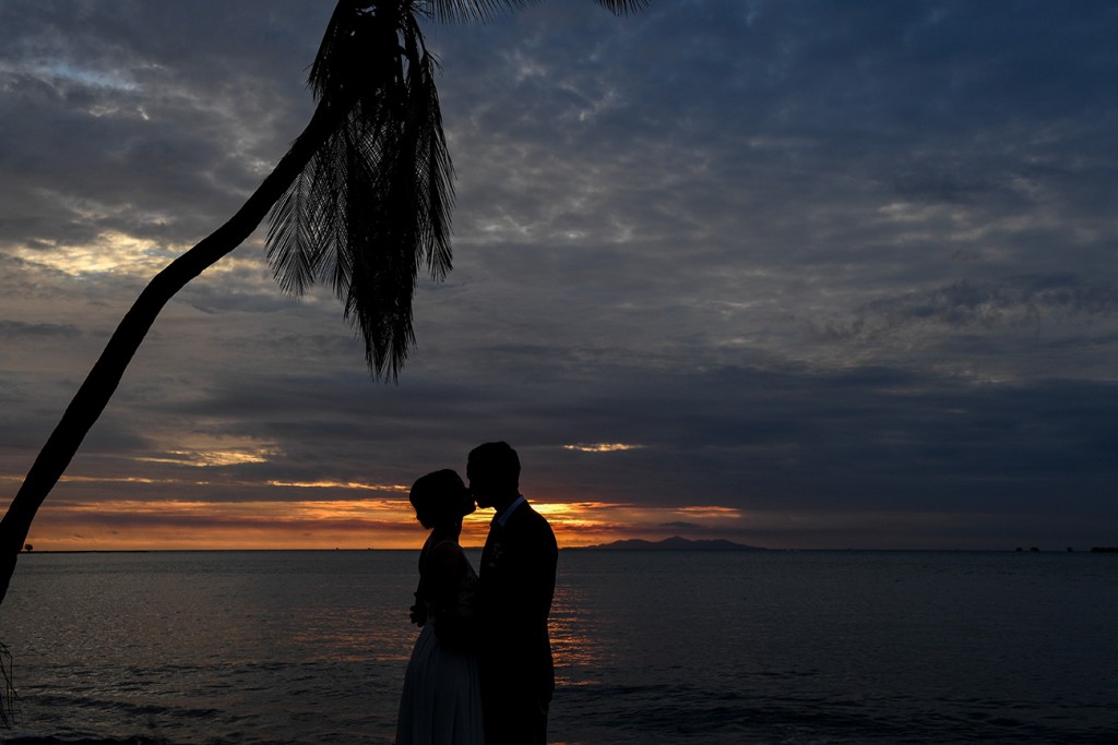 A silhouette of the couple kissing against the fiery sunset