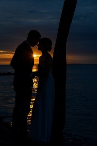 The couple is silhouetted by the fiery sun as they stand against a palm tree