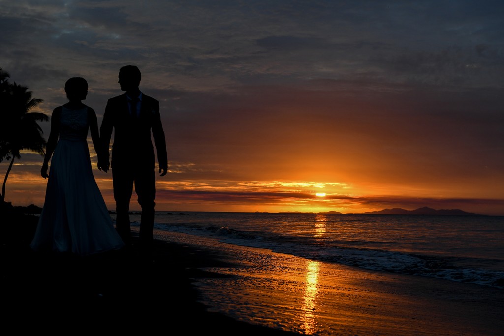 The couple is silhouetted as they stroll towards the fiery setting sun