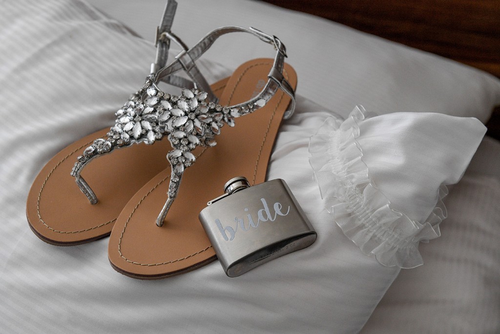 A cute and simple bridal liquor flask rests on simple flat bridal sandals