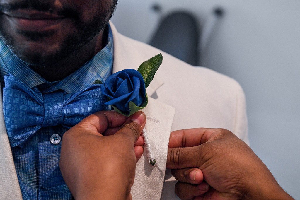 A closeup of a blue rose flower boutonniere being pinned on the grooms lapel
