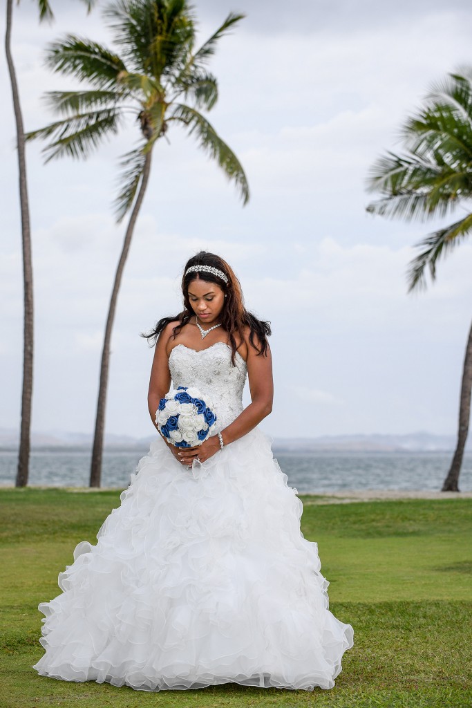 The stunning bride stands at the beach holding her blue and white rose bouqet