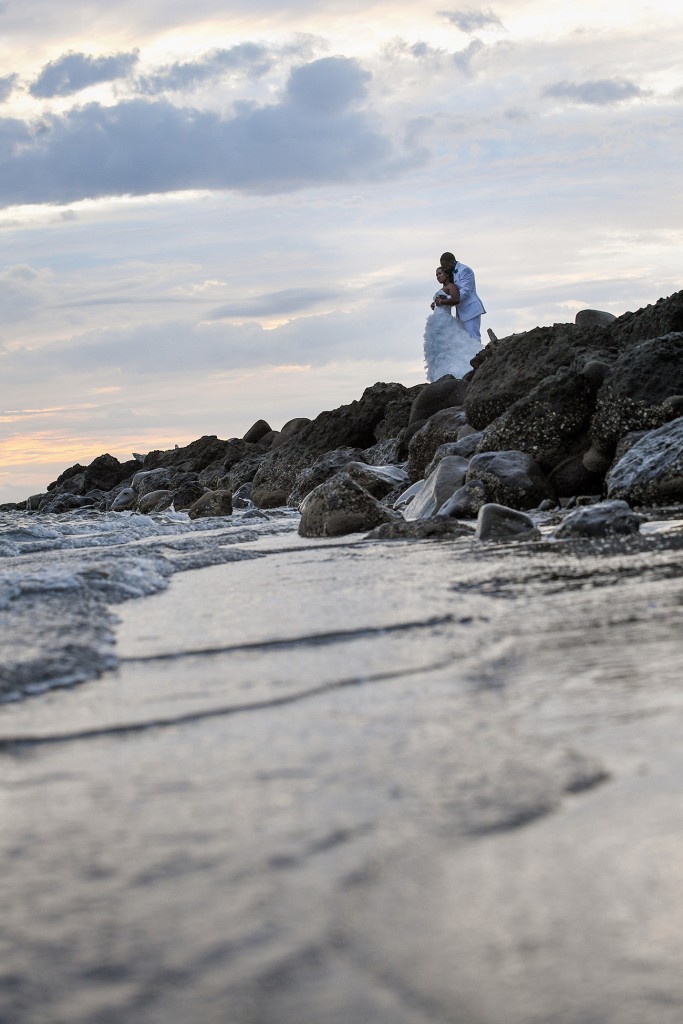 The bride and groom embrace on the rocky shore at sunset