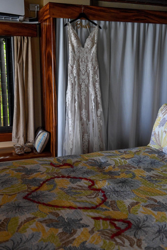 The bride's egg-white lace wedding dress hangs next to the bed
