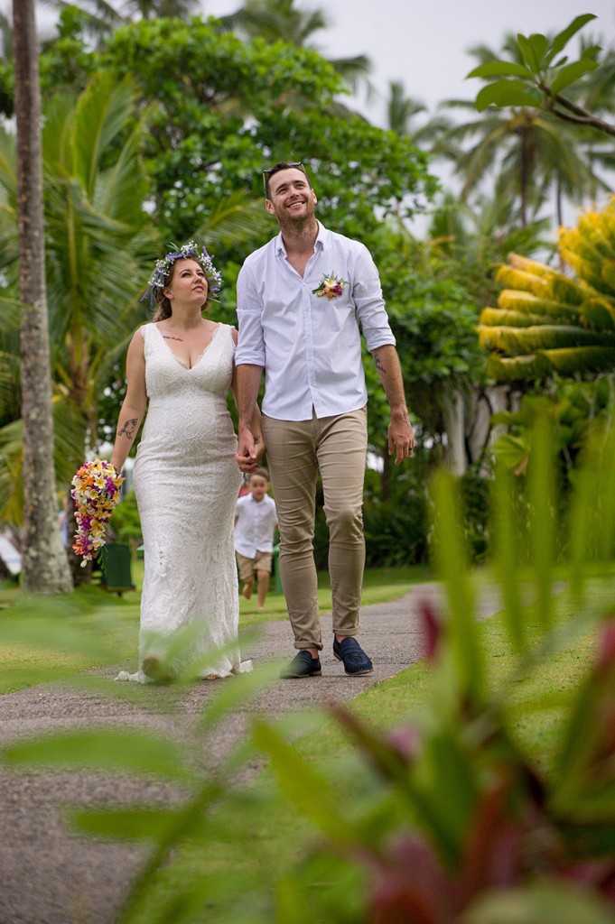 The bride and groom hold hands while walking through the greenery of Warwick Fiji
