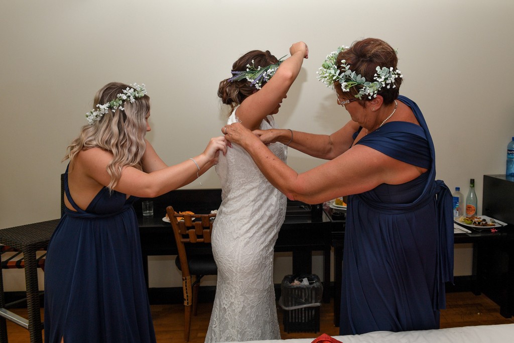 The bride's mother and a bridesmaid help the bride into her wedding gown