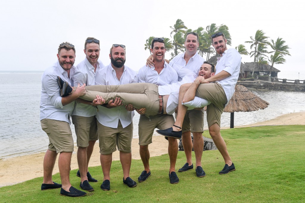 The groomsmen playfully carry the groom above the manicured grass