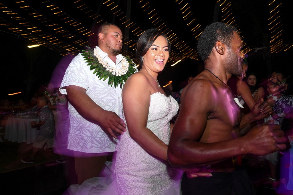 The newly weds dance with traditional Fiji dancers in a conga line under fairy lights