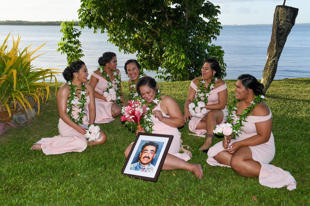 The bridesmaids laugh while seated on the grass seated on the grass against the stunning Pacific ocean