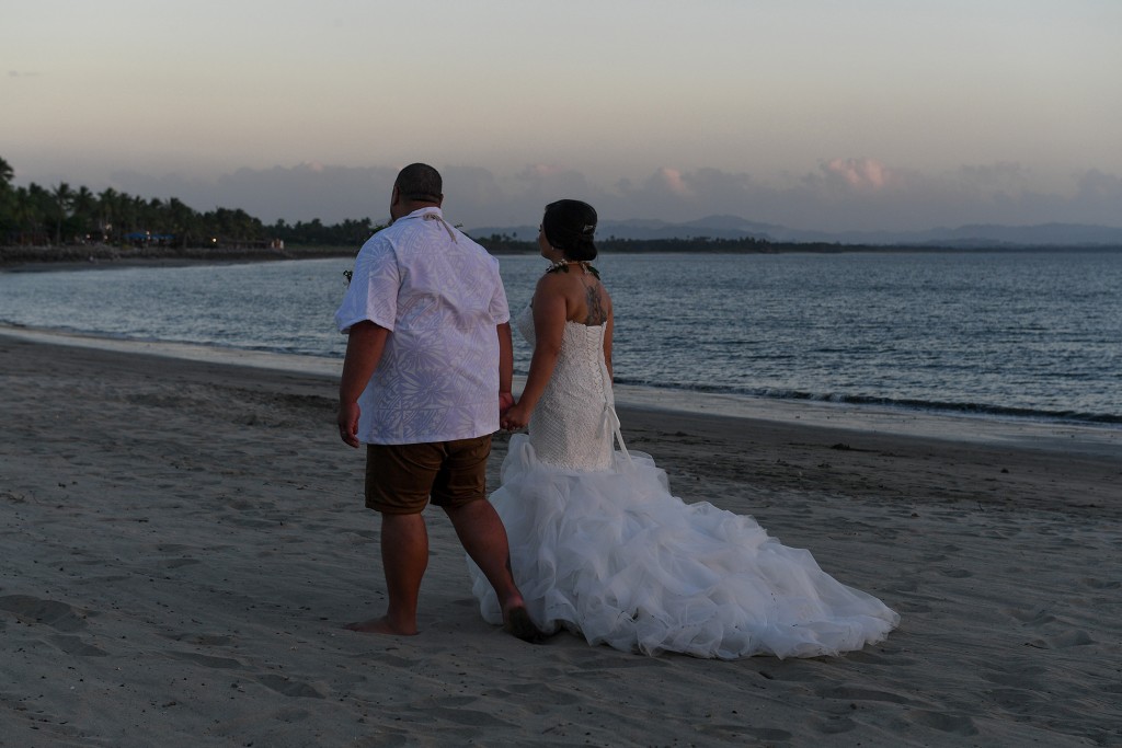 The newly weds stroll on the black sandy beach at sunset