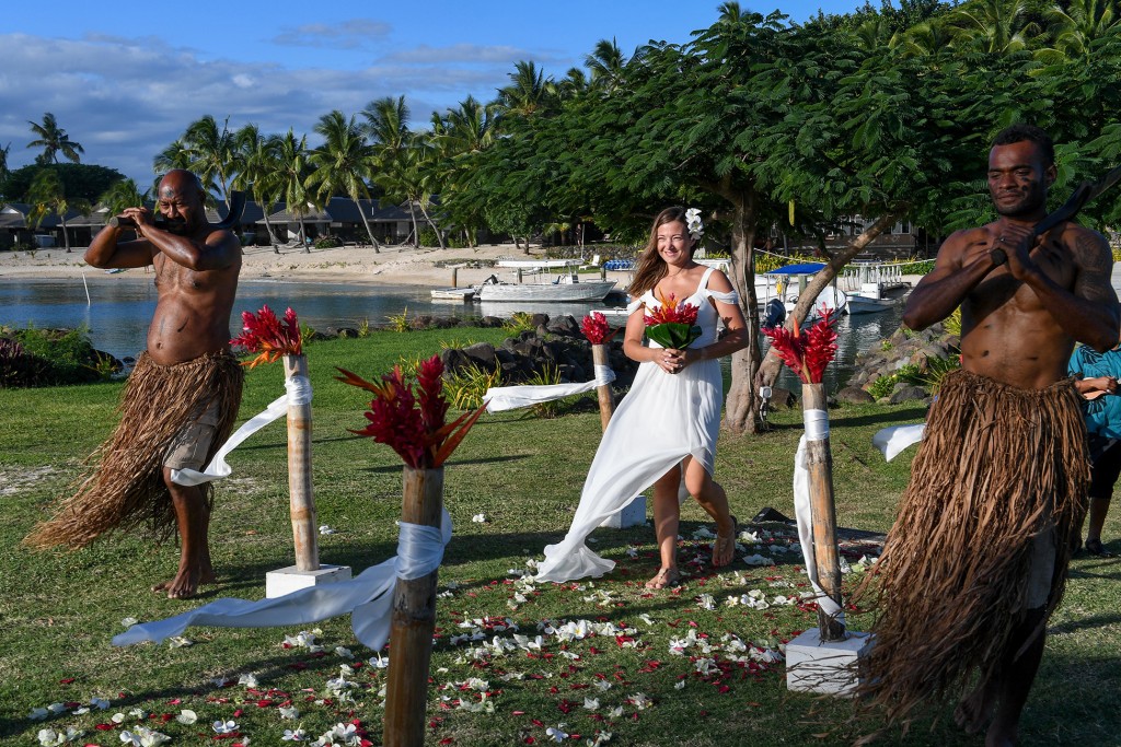 The stunning bride walks down the aisle escorted by traditional Fiji dancers