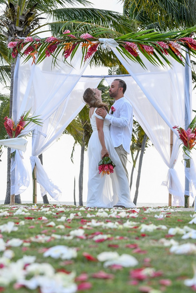 The married couple laugh under the arch altar made of ginger flowers and rose petals on the aisle