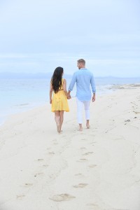 The couple strolls hand in hand against baby blue sand