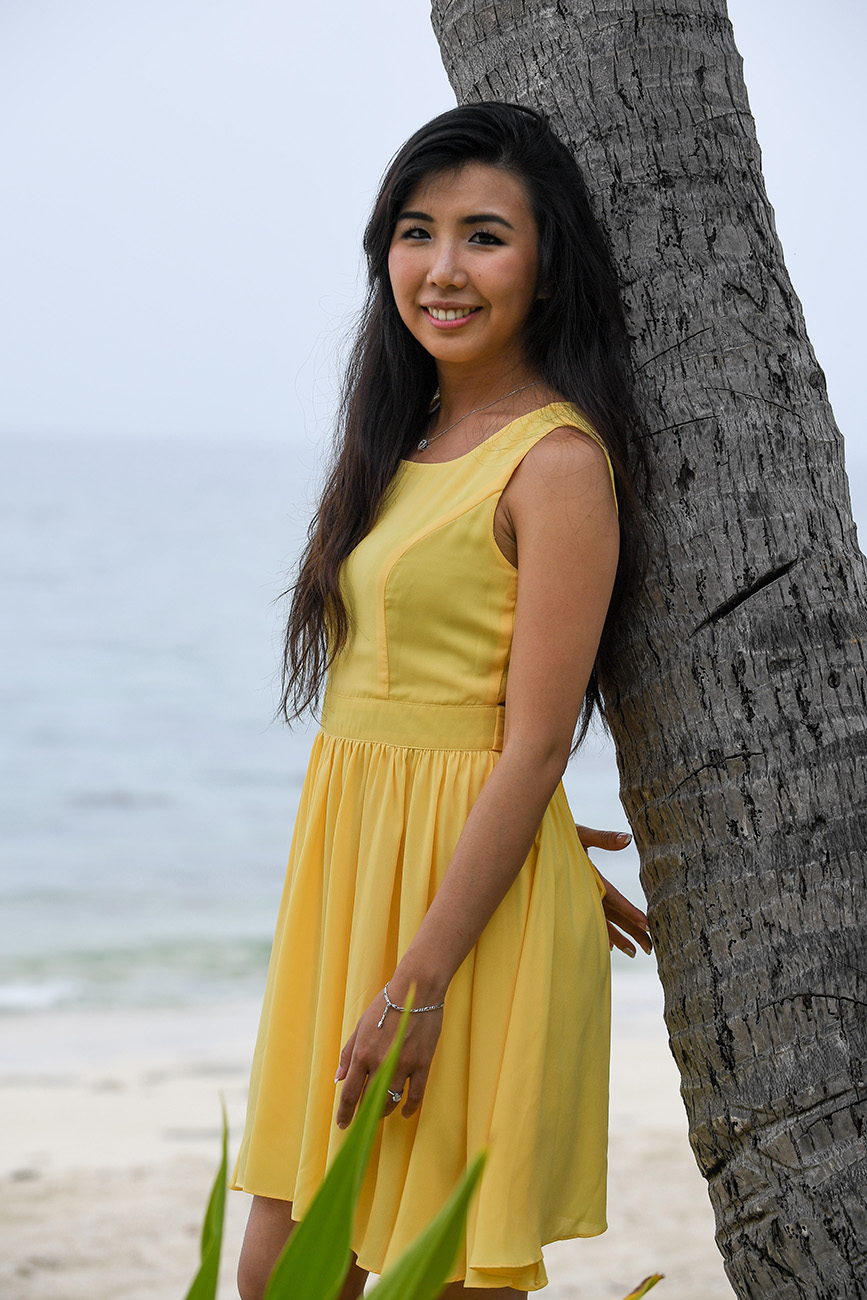 The bride-to-be dressed in a bumbleebee yellow dress leans against a palm tree