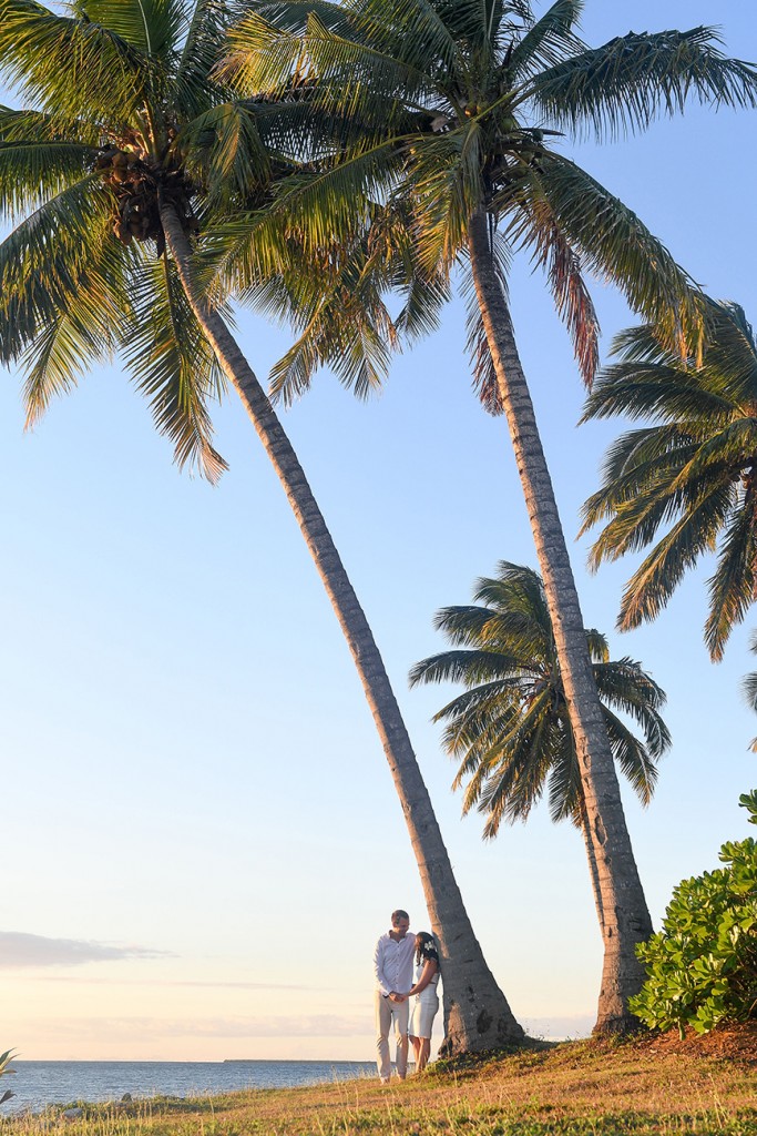 The couple cosies up against gigantic palm trees on the beach