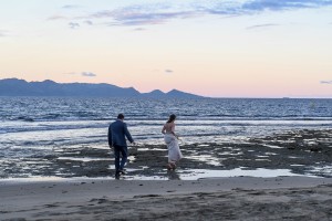 The couple walks on the wet beach at sunset