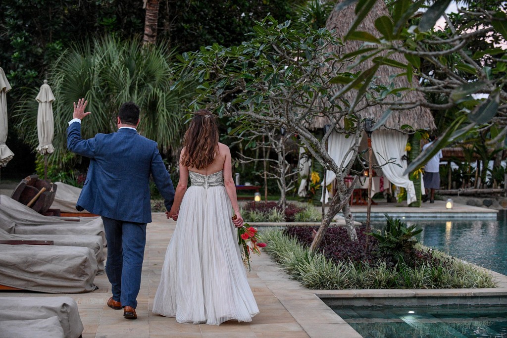 The newly weds wave as they stroll beside their personal pool