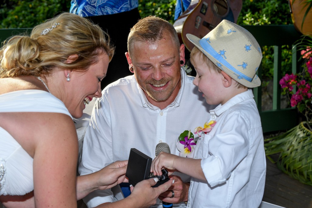 The bride and groom smile with their son who presents their rings