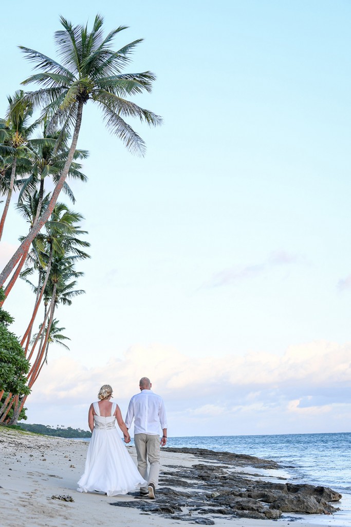 The newly weds stroll on the beach under palm trees in Shangri La Fiji
