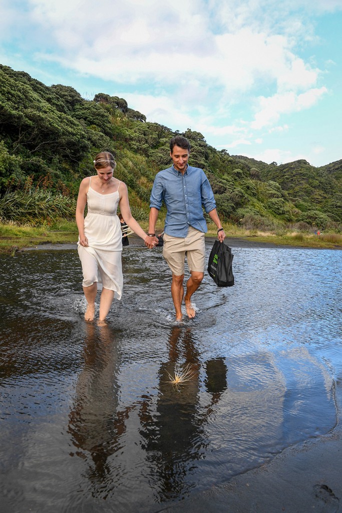 The married couple wade through the shallow waters at Karekare black sand beach