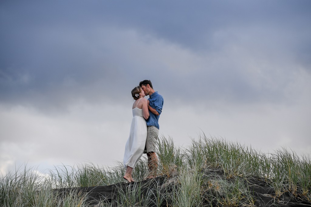 The married couple kiss on a hill against a deep grey sky
