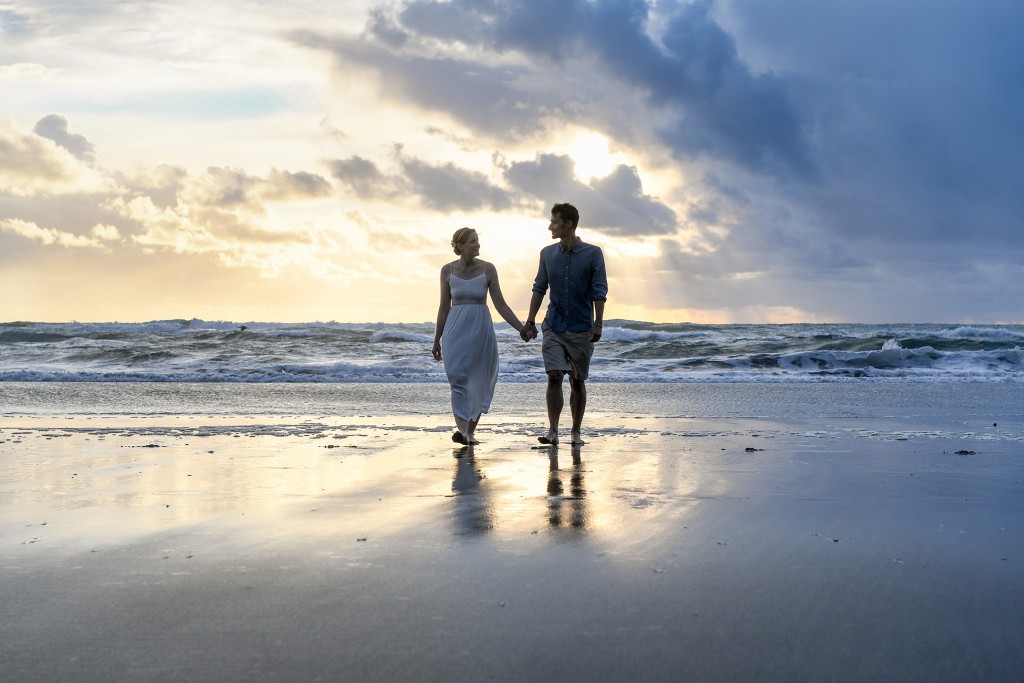Newly weds walk against a golden sunset in the horizon
