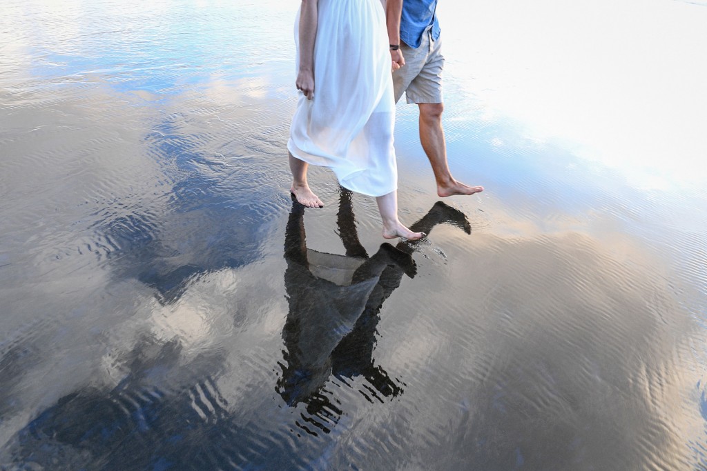 A reflection of the newly weds walking on sand in Karekare