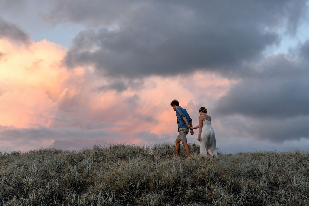 The newly weds walk over a hill at Karekare during sunset