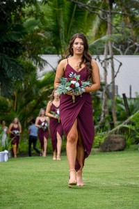 A stunning bridesmaid in a burgundy dress walks down the aisle