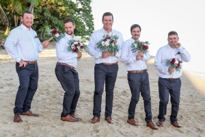 The groomsmen pose with flowers on the beach