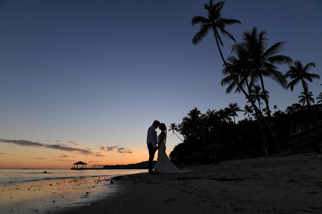 A silhouette photo of the newly weds and the palm trees at sunset