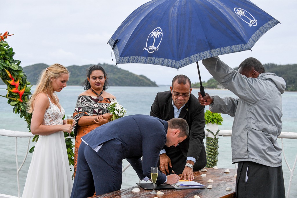 The groom signs the marriage certificate under the umbrella
