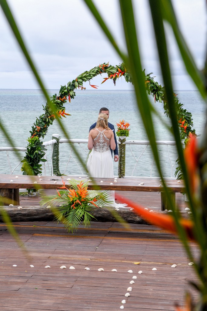 A peek through palm fronds of the newly weds at the beach view altar