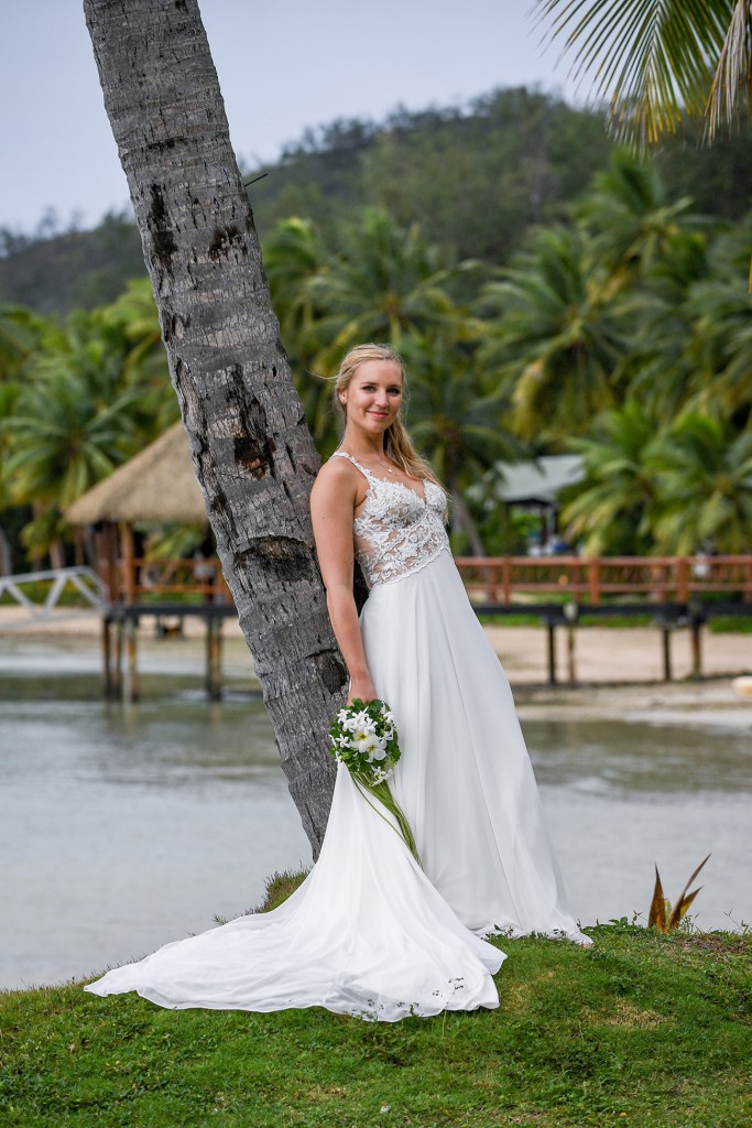 The bride leans against a towering Fiji palm tree
