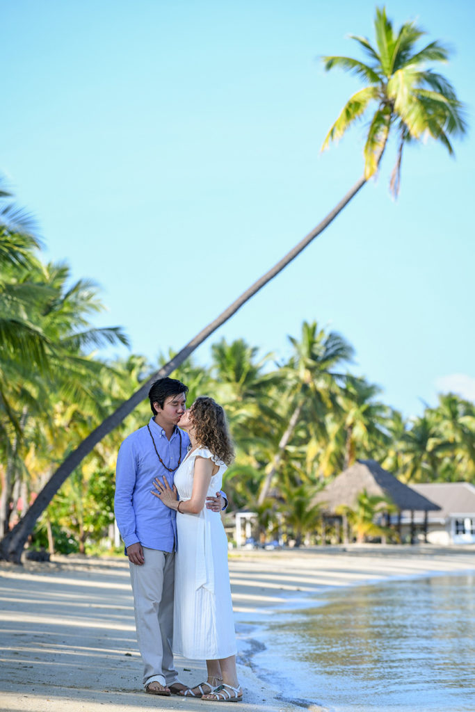 The loving couple shares a passionate kiss on the beach against towering Fiji palms
