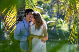 The groom whispers sweet nothings into his bride's ear while leaning against Malolo Island palm trees