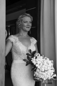 A monochrome portrait of the bride in the doorway holding a white frangipani bouquet