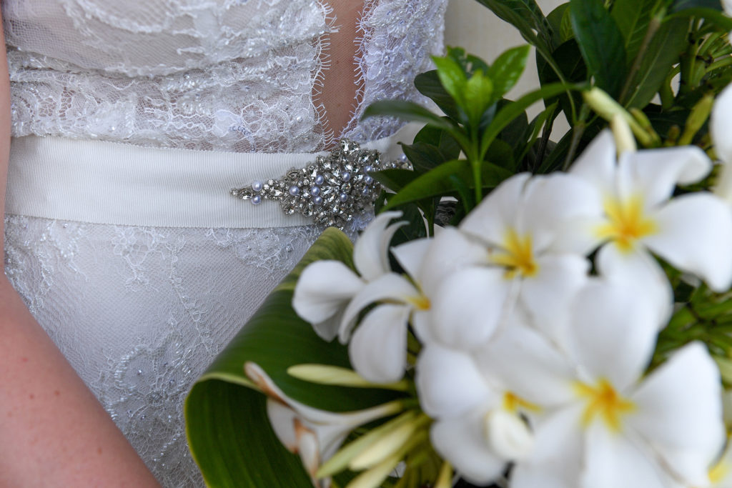 Detail of the bride's diamond waist brooch against white frangipani flowers