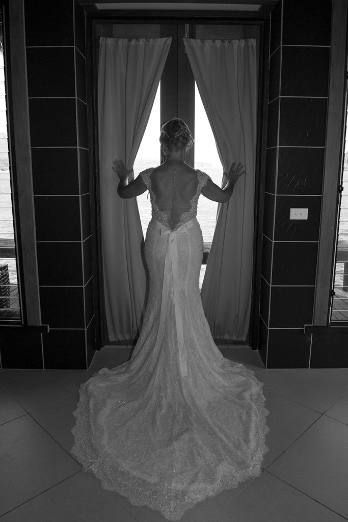 A monochrome image of the bride posing in the window with her bareback wedding gown