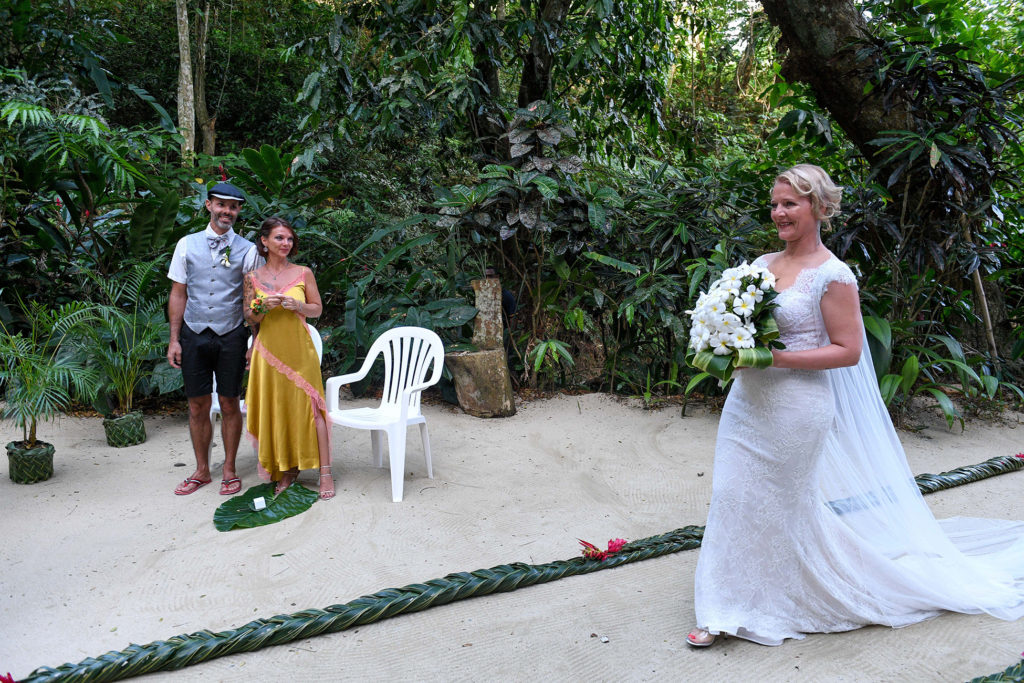 The bride walks down the sand aisle as wedding guests watch
