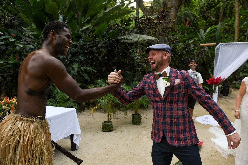 The groom high fives and laughs with a traditional Fiji warrior