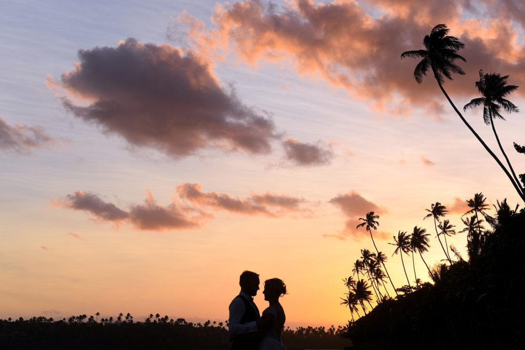 A silhouette of the newly weds under Fiji palms and a sunset