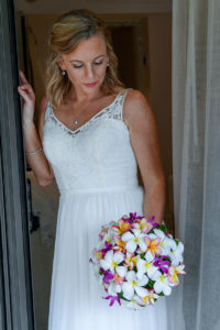 The stunning bride poses in the doorway holding her multicoloured bouquet