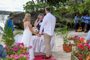 The bride and groom hold hands at the beachside altar overlooked by Shangri La